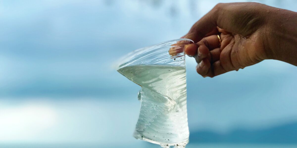Plastic in the ocean page banner: a hand holding up plastic outside
