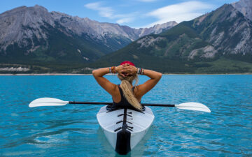 Girl in ocean on a kayak looking up at mountains