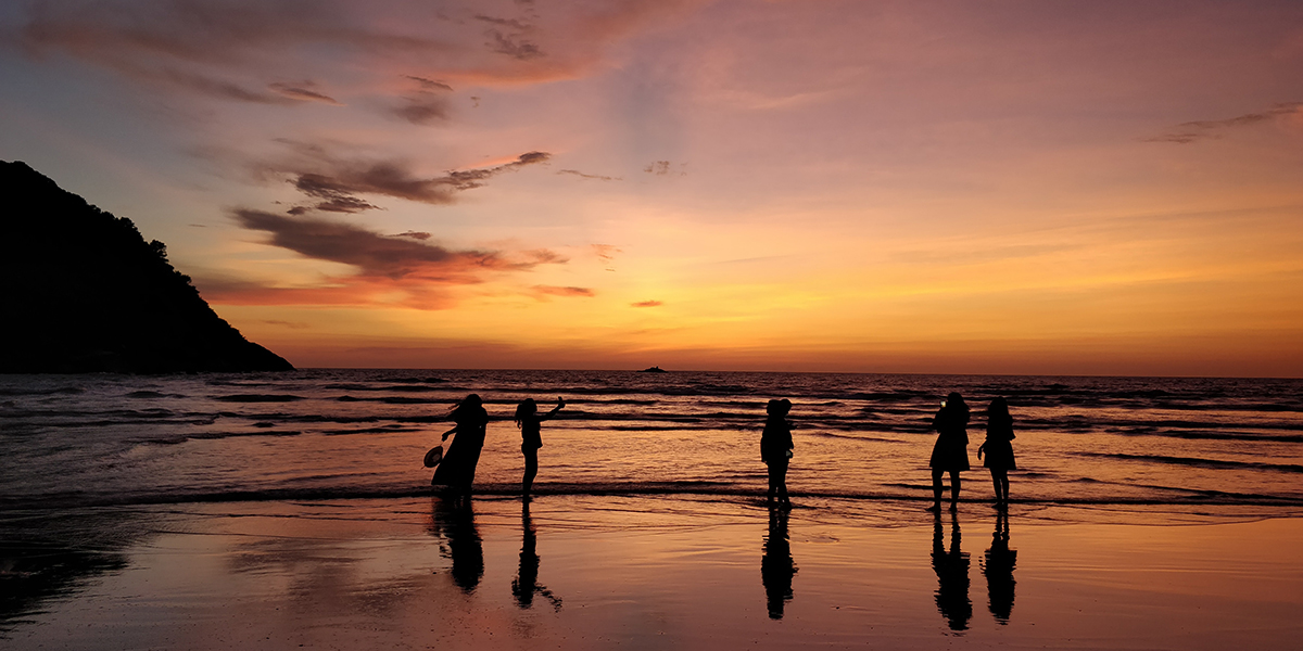people standing on beach at sunset