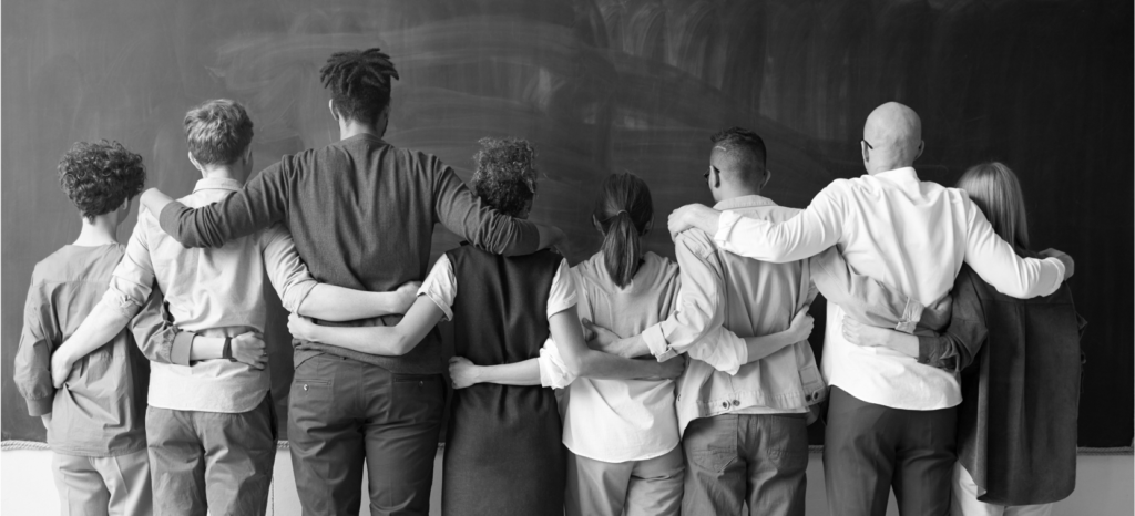 A black and white image of people standing with their arms around each other.