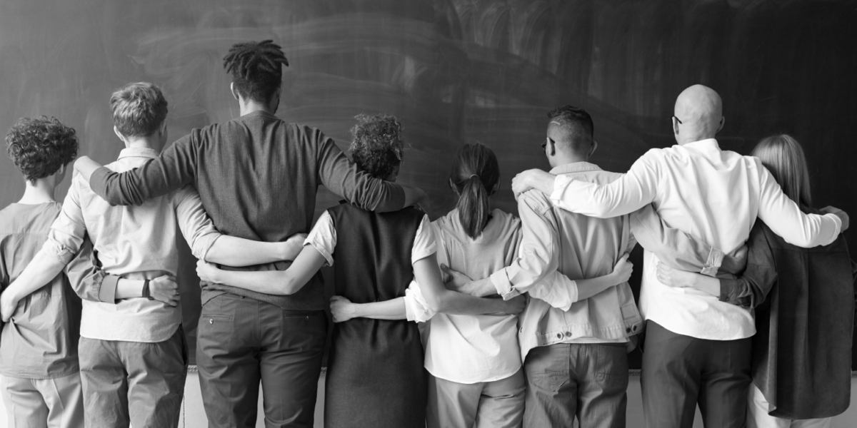 A black and white image of people standing with their arms around each other.