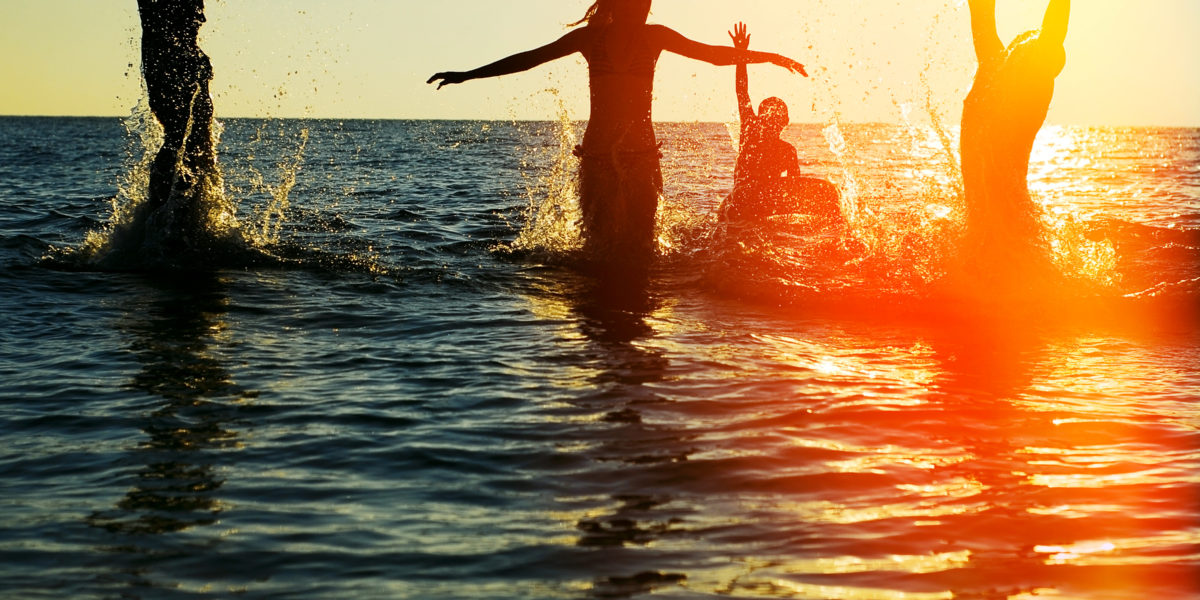 Young Writers Banner: Silhouettes of young group of people jumping in ocean at sunset