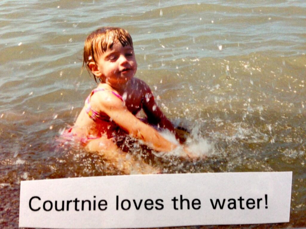 Courtnie Park as a young toddler splashing in the water, with a piece of paper over top of the picture that says "Courtnie loves the water!"