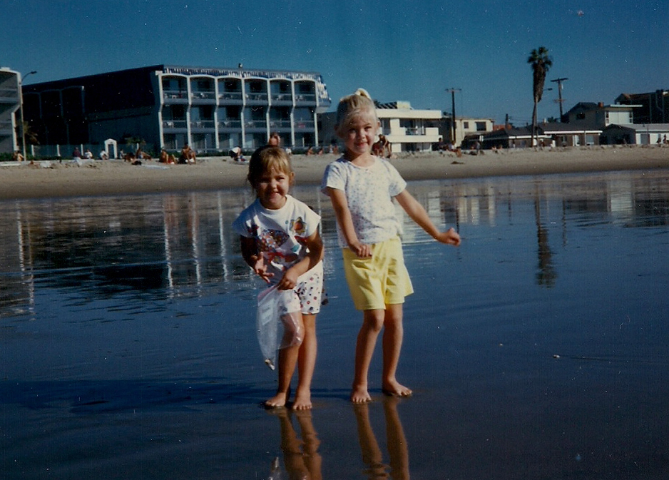 Kaitlyn and her sister standing and smiling as children at Huntington Beach