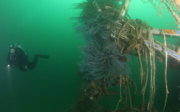 A diver swims near a wreck draped with lost fishing nets. Photo: NOAA