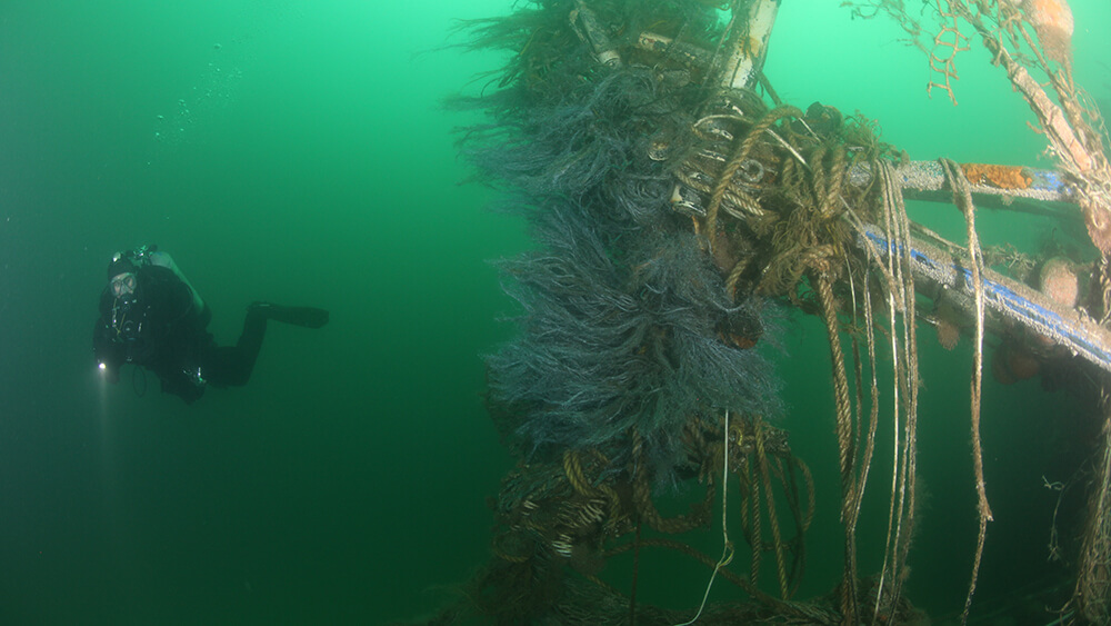 A diver swims near a wreck draped with lost fishing nets. Photo: NOAA
