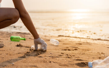 a woman picking up plastic pollution along the beach