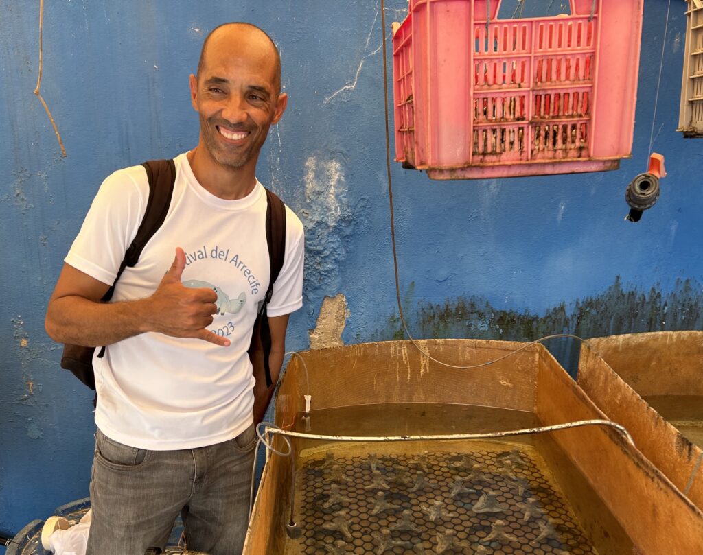 Dr. Pedro Chevalier-Monteagudo giving a thumbs-up at the Acuario Nacional with coral substrates next to him.