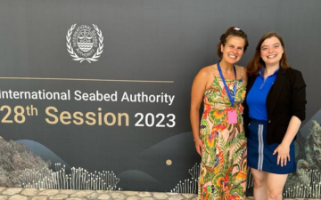 Bobbi-Jo Dobush and Madeline Warner standing in front of the International Seabed Authority's banner during a meeting