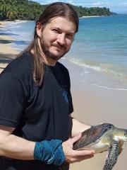 Jaime Restrepo holding a green sea turtle on a beach.